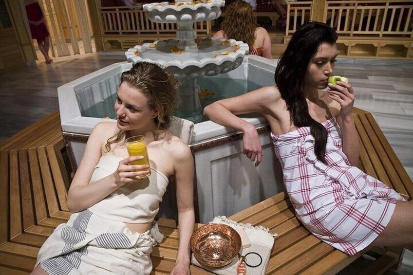 Two women sitting on wooden chairs by a poolside, holding drinks. 4