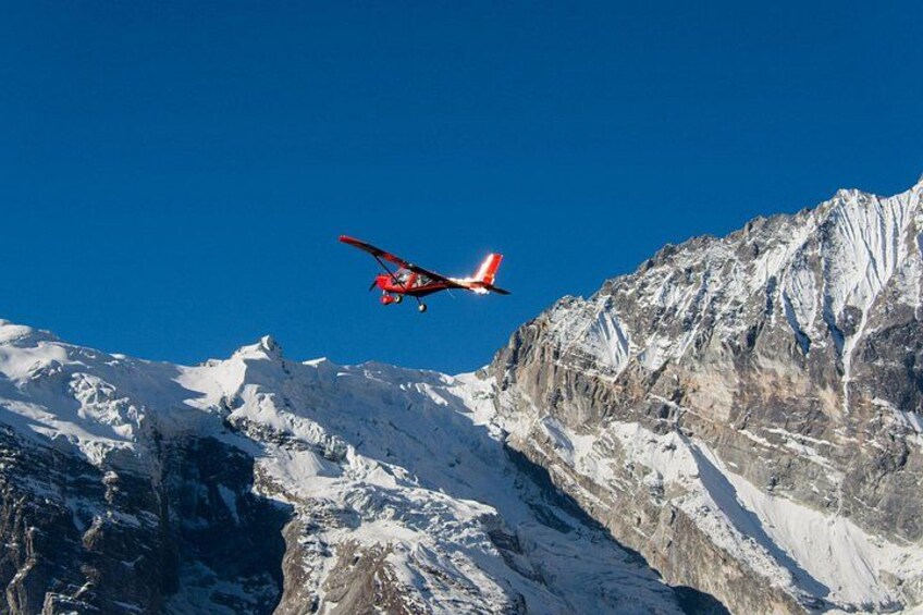 A red and white aircraft flying over snow-covered mountains under a clear blue sky. 3