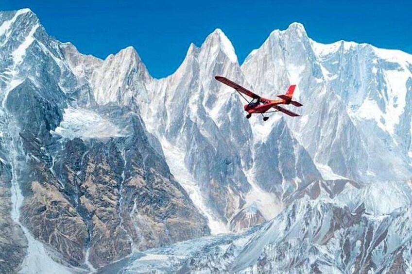 A red biplane flying over snow-capped mountains. 1