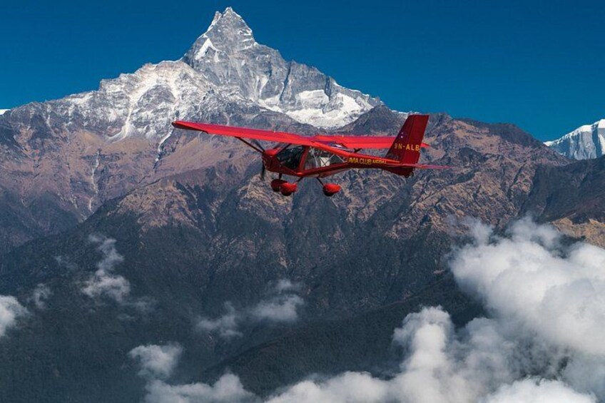 A red biplane flying over a mountainous landscape with a snow-capped peak in the background. 2