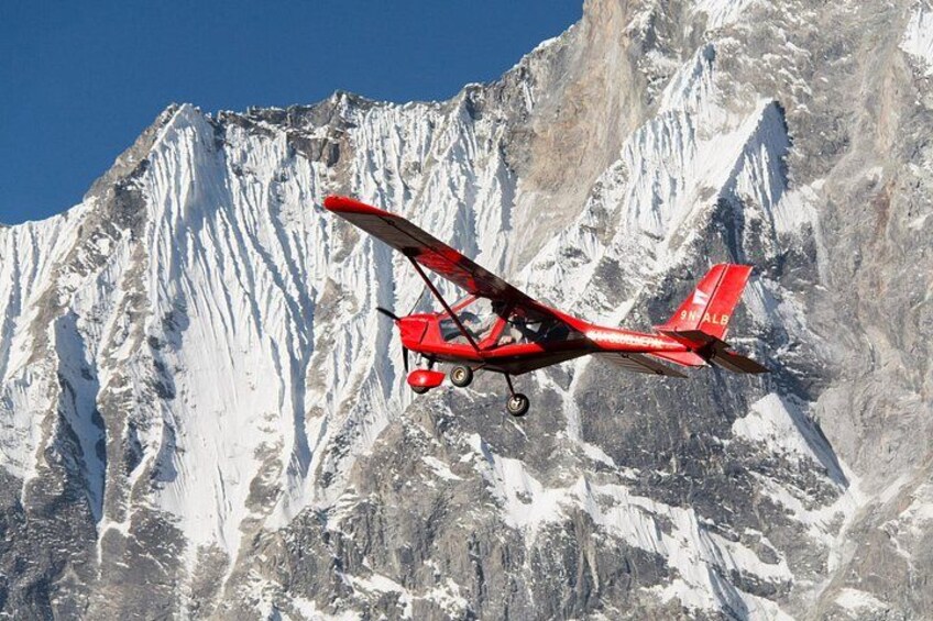 A red biplane flying over a snow-covered mountain range. 4