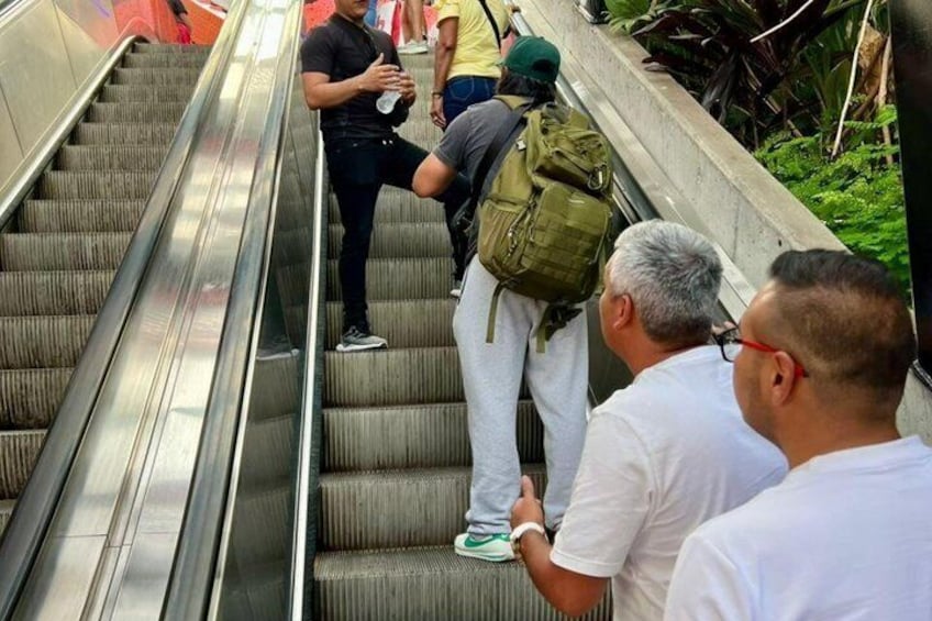 Un groupe de personnes se trouve sur un escalier mécanique, et certaines d’entre elles portent des sacs à dos. 3