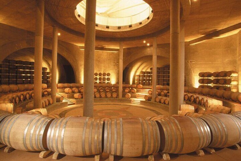 A wine cellar with wooden barrels arranged in a circular pattern, supported by columns, and illuminated by a central light fixture. 3