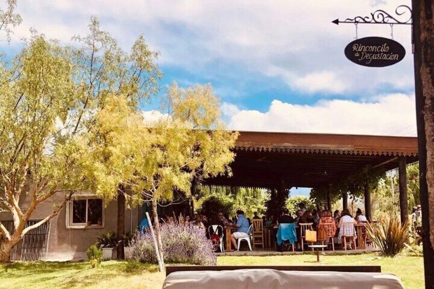 A covered outdoor seating area with people dining, a sign reading "Rincón de Degustación," and a building in the background. 2