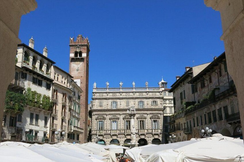 Un edificio storico con una torre dell'orologio, circondato da tavoli coperti e altri edifici. 3