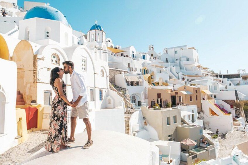 A couple embracing on a white-washed street with blue-domed buildings in the background. 5