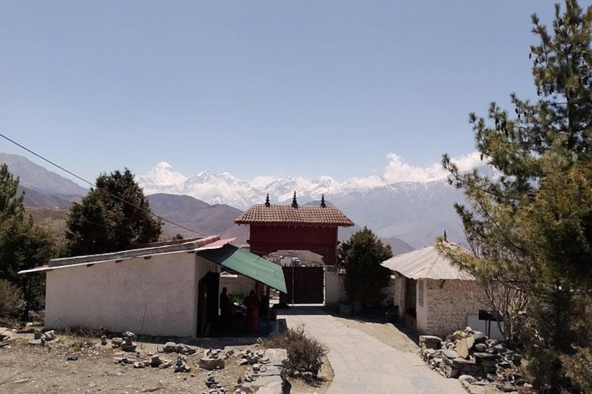 A rural village with a prominent red-roofed building, a dirt path leading to it, and snow-capped mountains in the background. 4
