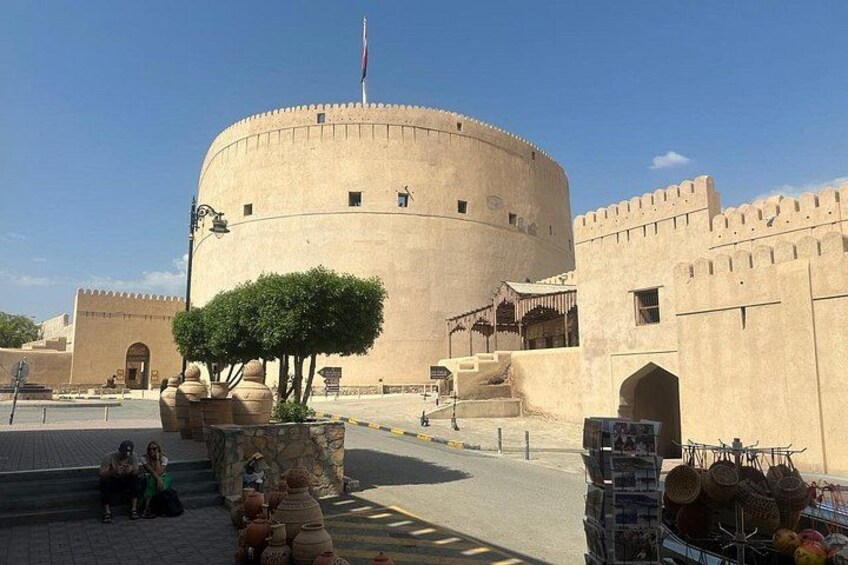 A historic building with a round tower, a flag, and a traditional market area with stalls. 1
