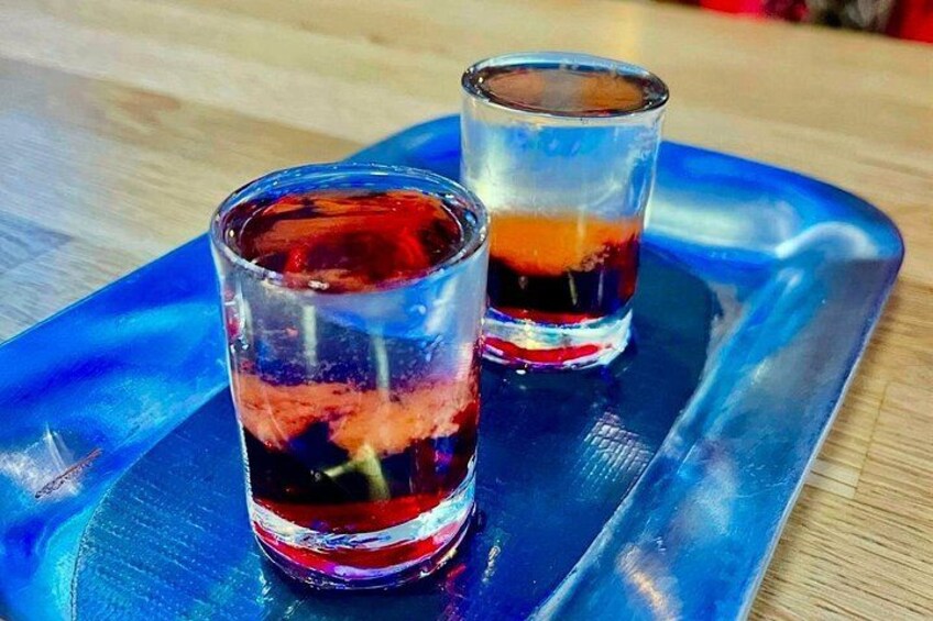 Two shot glasses with a dark liquid on a blue tray. 2