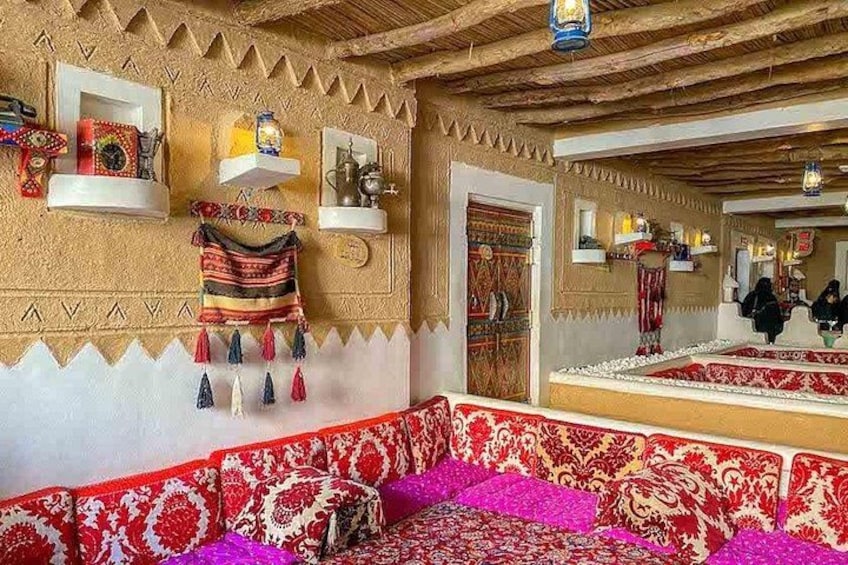 A traditional interior with patterned rugs, a hanging tapestry, and shelves with decorative items. 2
