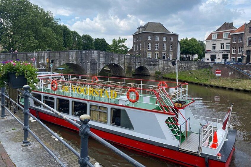 A red and white riverboat named 'The First' docked at a canal with a stone bridge in the background. 4