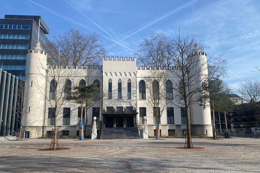A castle-like building with arched windows and a central tower, surrounded by bare trees and a paved area. 3
