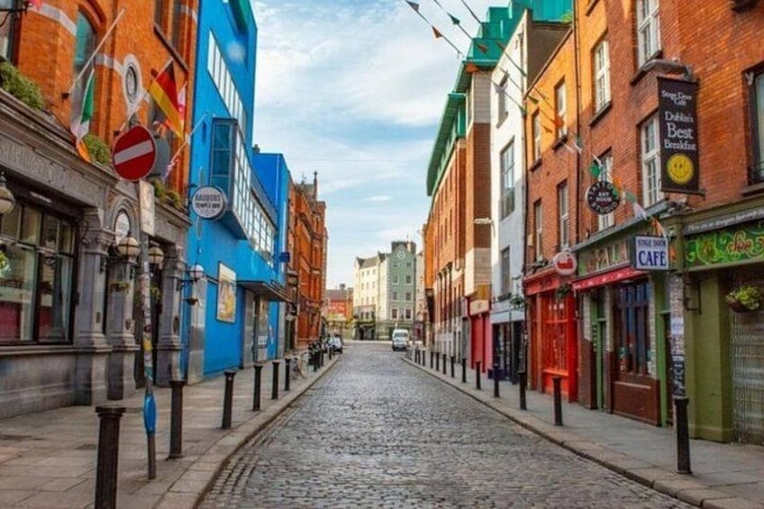 Una calle empedrada flanqueada por edificios coloridos, una señal de prohibido el paso y una cafetería. 1