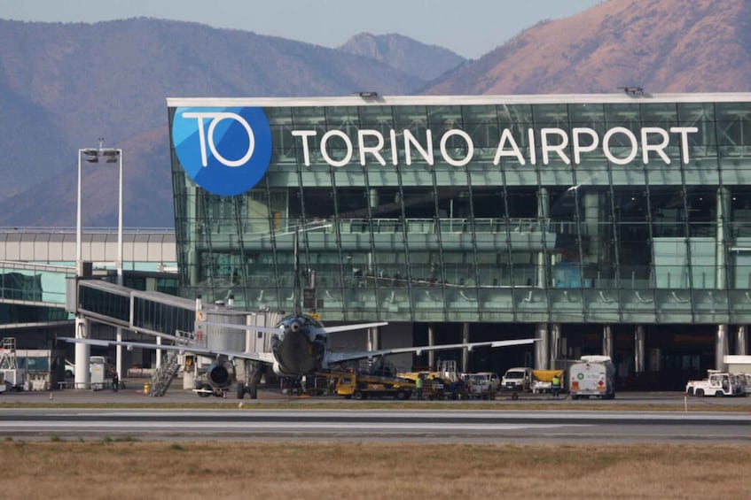 The exterior of Torino Airport with a large glass building and a sign reading "TORINO AIRPORT". 4