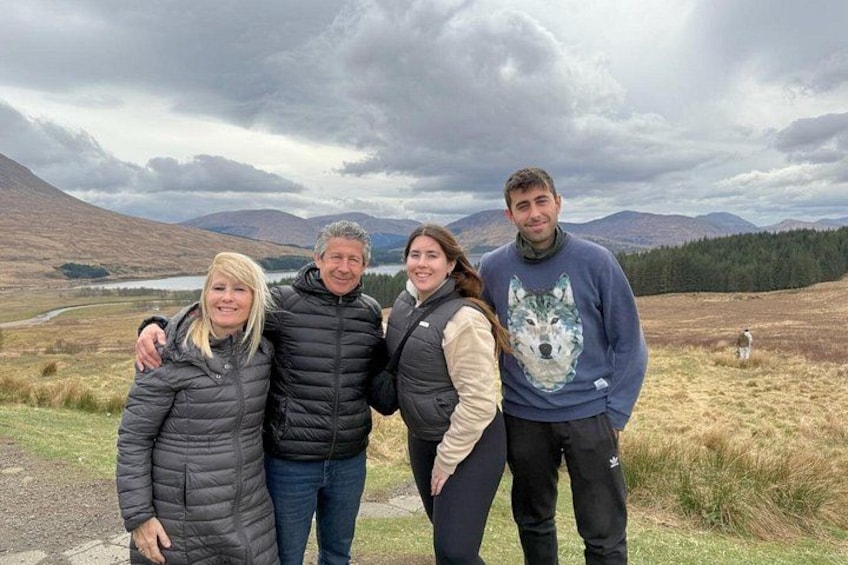 Four people standing in a grassy field with mountains in the background. 2