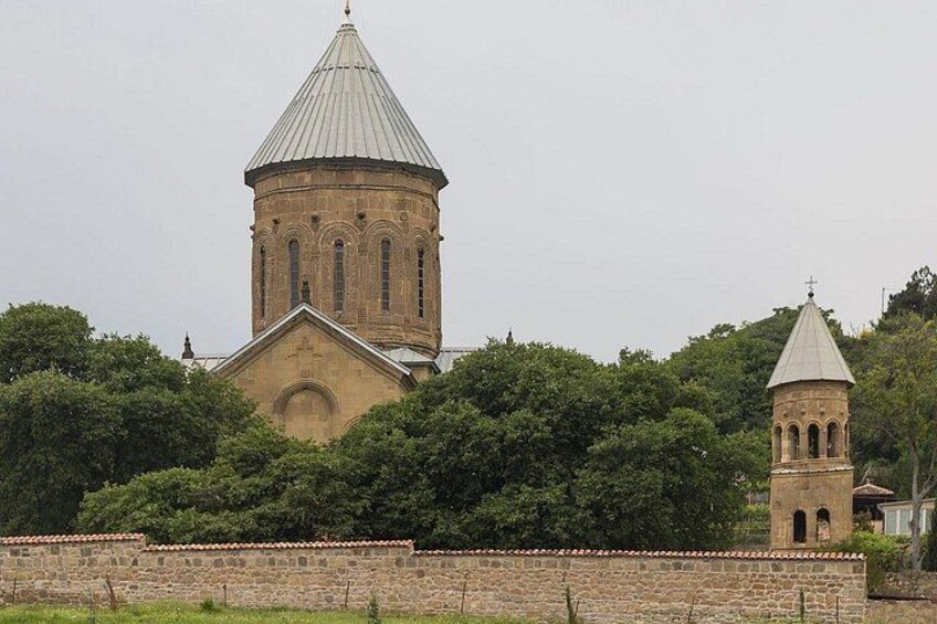Una iglesia con un campanario y una cúpula, rodeada de árboles y un muro de piedra. 1