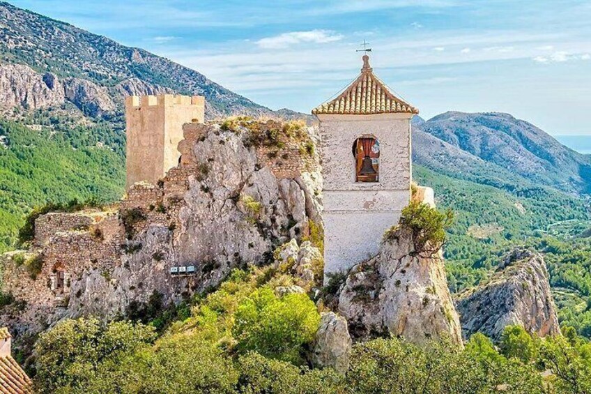 A historical stone tower and ruins on a hill with lush greenery and mountains in the background. 5