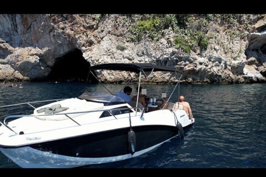 A boat with two people, a rocky coastline, and a cave entrance. 2