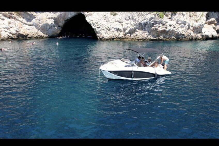 A boat anchored near a rocky coastline with a cave entrance. 4