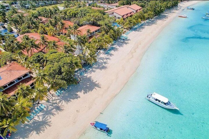 Una playa con agua turquesa cristalina, un bote y una hilera de edificios con tejados rojos. 4