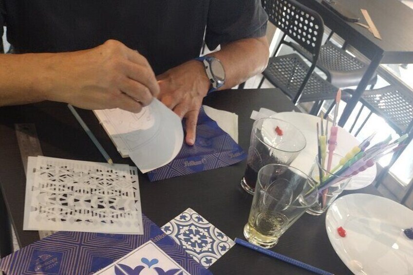 A person at a table with a blueprint, a glass of water, and a cup with pens. 3
