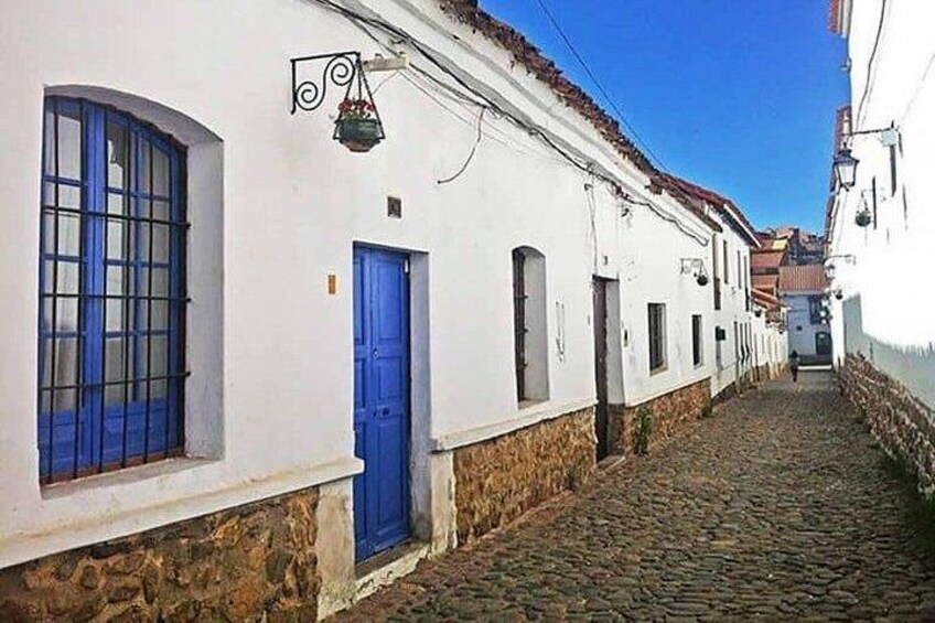 A cobblestone street lined with white buildings, blue doors, and a clear blue sky. 2