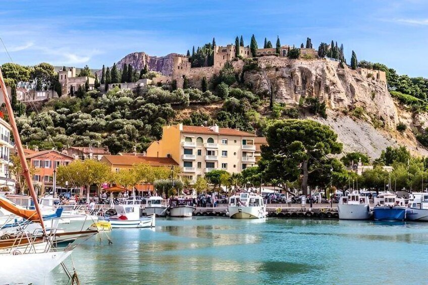 A coastal town with boats docked, a historic fort on a hill, and buildings along the waterfront. 2