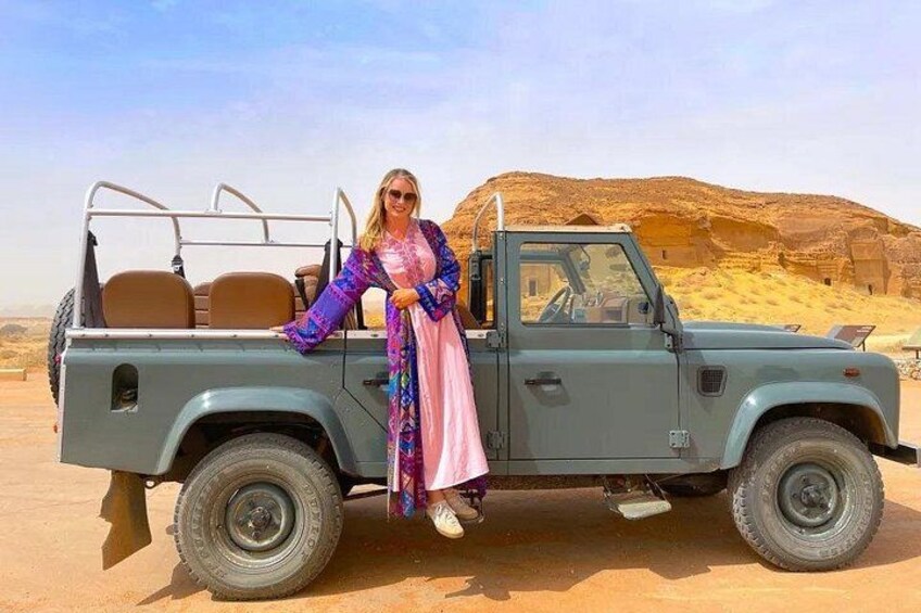 A person in a long dress sitting in a light blue off-road vehicle with a desert landscape in the background. 5