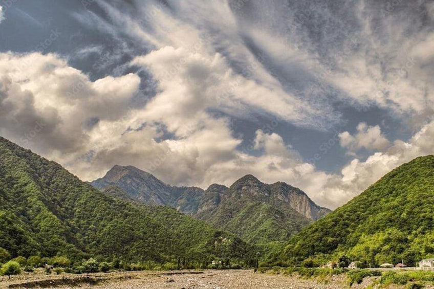 A mountainous landscape with dense green vegetation and a clear sky with clouds. 3