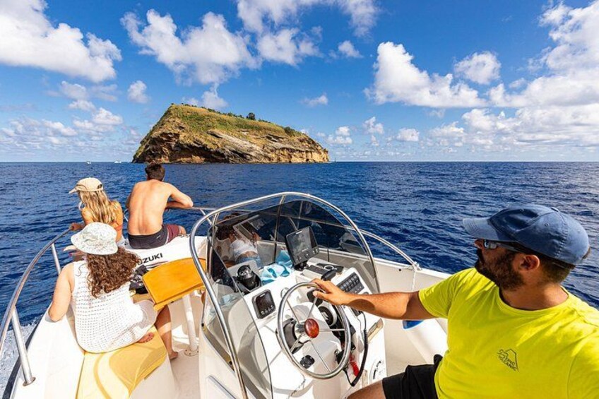 A boat with people on a clear day, a rocky island in the distance, and a blue sky. 3