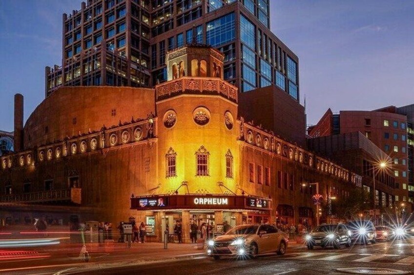 A historic theater with 'ORPHEUM' signage, surrounded by modern buildings and busy streets at dusk. 3