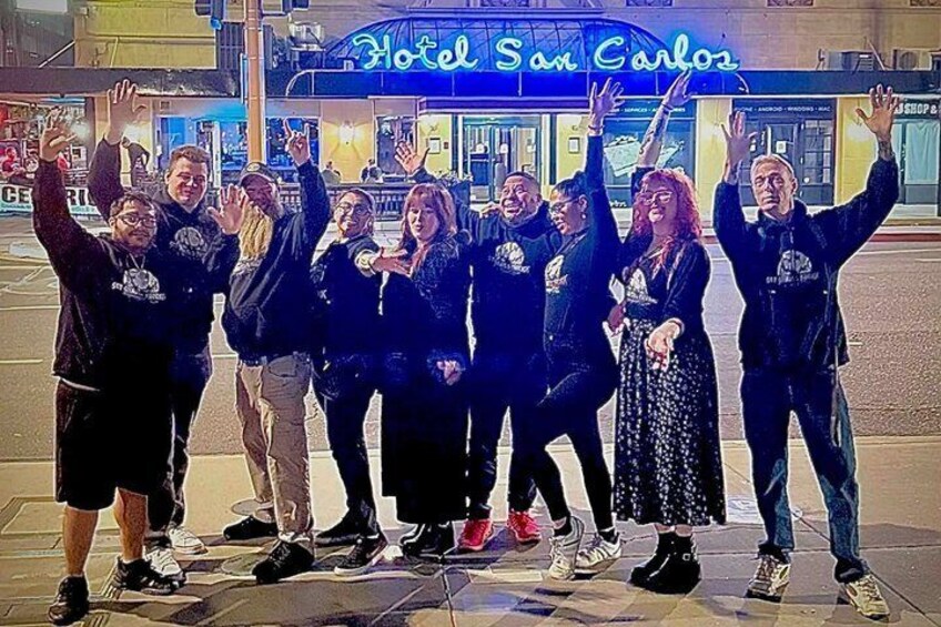 A group of people posing in front of a building with a neon sign that reads 'Hotel San Carlos.' 2