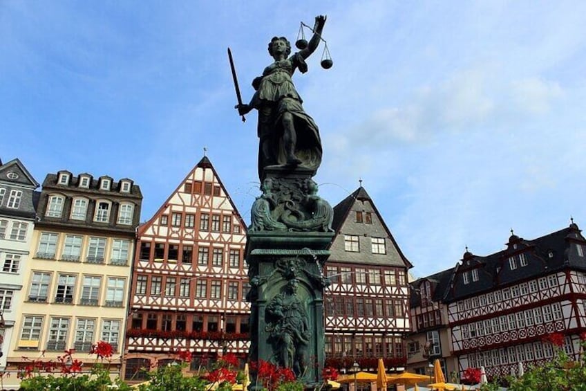A statue of a woman holding scales and a sword, surrounded by traditional half-timbered buildings. 3