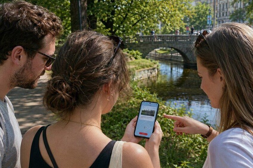 Trois personnes regardent un smartphone, avec un pont et de l’eau en arrière-plan. 5