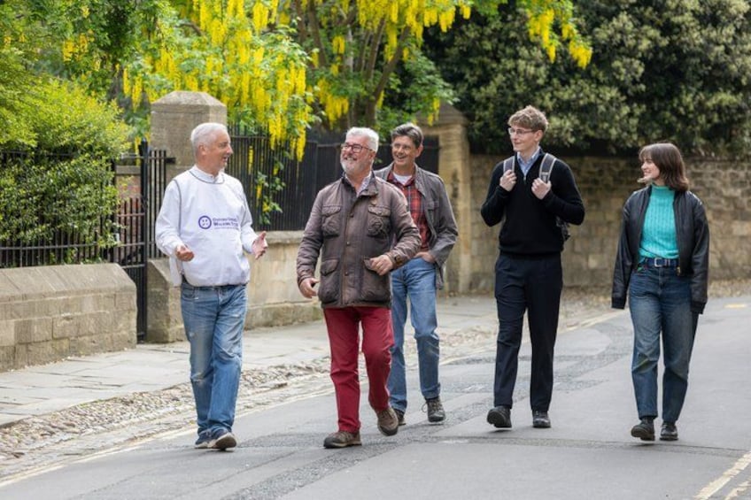 A group of people walking on a paved path, surrounded by greenery and a stone wall. 1