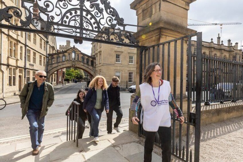 A group of people walking through a historic gate with ornate ironwork, leading to a building with classical architecture. 5