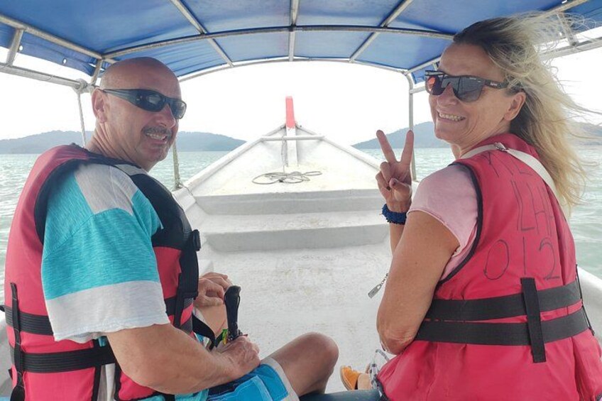 Two people on a boat wearing life jackets, with a body of water and distant land in the background. 2