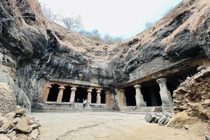 A rock-cut temple with columns, a person standing in front, and a clear sky. 1