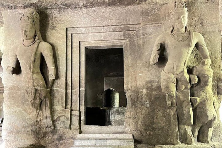 A stone carving of a figure with a child, a doorway, and a small step leading into a dark interior. 2