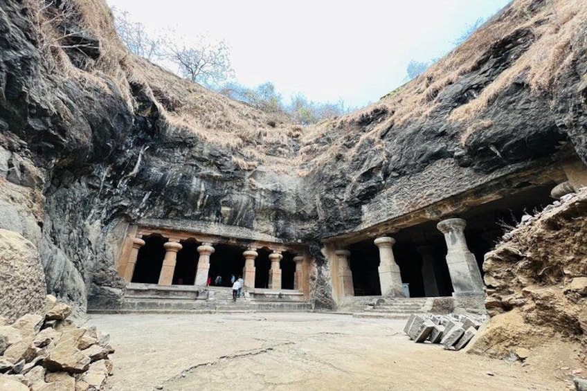 Un temple taillé dans la roche, orné de colonnes, avec une personne debout devant et un ciel dégagé. 1