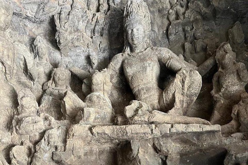 A stone carving of a seated figure with a staff, surrounded by smaller figures in a cave. 2