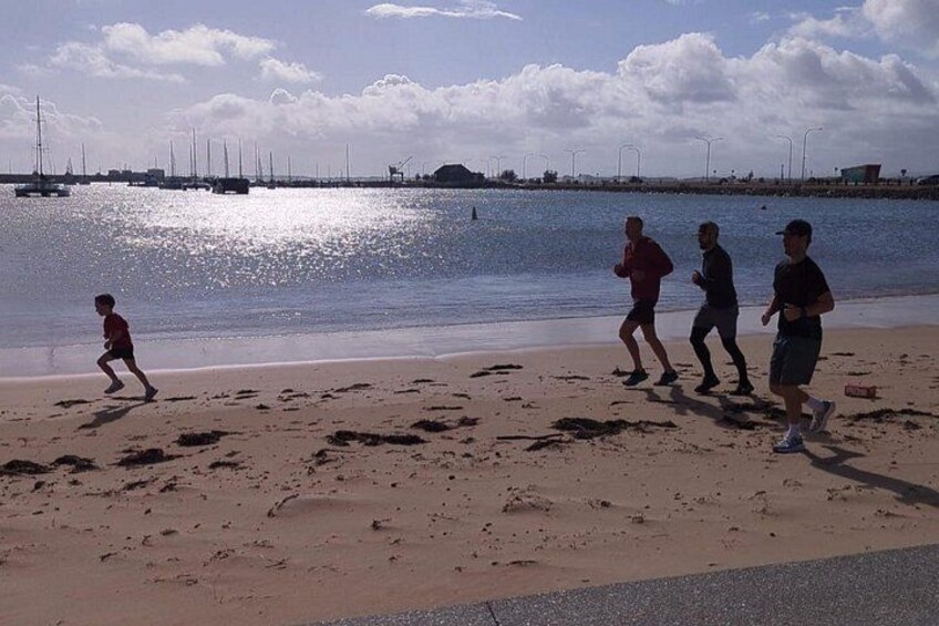 A beach with people jogging, a calm sea, and sailboats in the distance. 2