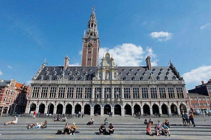 Un bâtiment historique doté d’une tour imposante, une vaste place ouverte où les gens sont assis et se promènent, et un ciel d’un bleu éclatant. 4