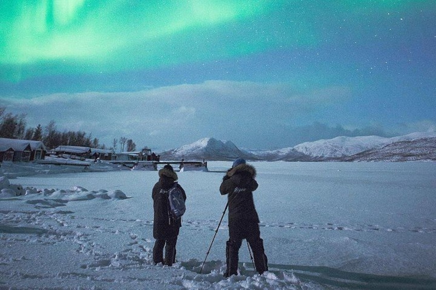 Two people standing on a frozen lake, looking at the sky. 3