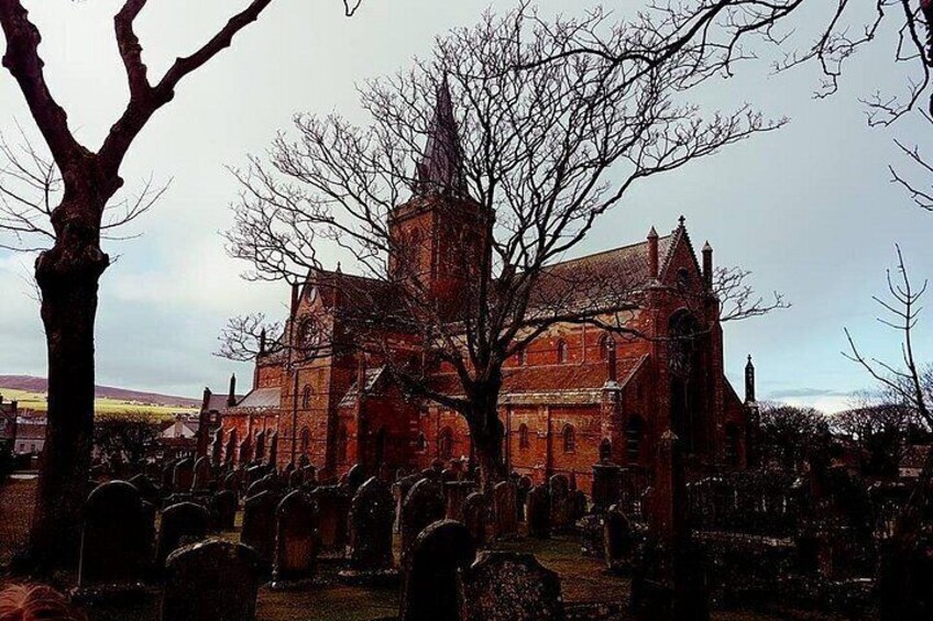 Eine große Backsteinkirche mit einem markanten Turm, umgeben von einem Friedhof mit zahlreichen Grabsteinen. 2