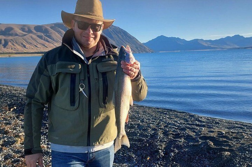 A person holding a fish by a lake with mountains in the background. 4