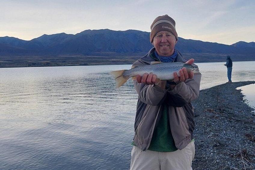 A person holding a fish by a lake with mountains in the background. 3