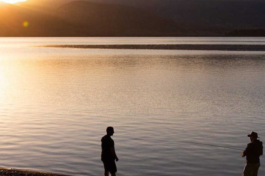 Two people fishing by a calm lake at sunset. 2