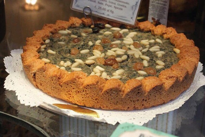 Ein runder Kuchen mit goldbrauner Kruste, belegt mit Nüssen und getrockneten Früchten, präsentiert auf einer weißen Häkeldecke. 4