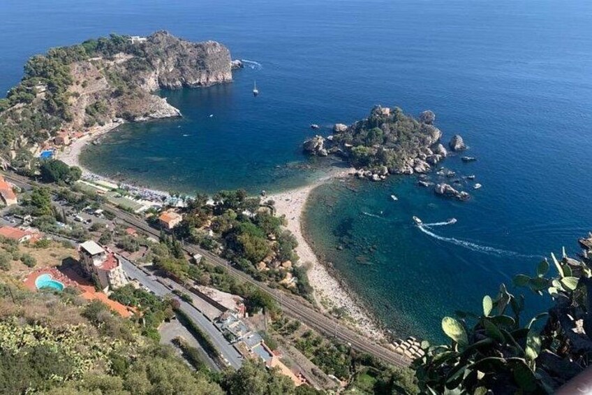 A coastal landscape with a beach, rocky outcrops, and a clear blue sea. 2